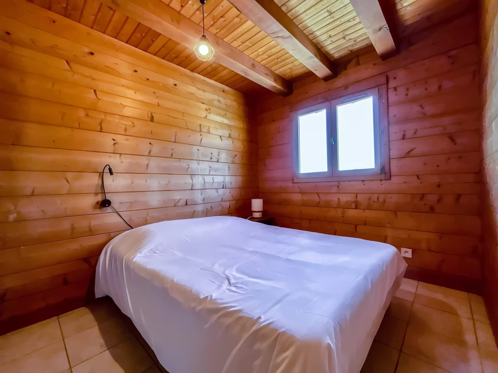 Chambre avec lit double, draps blancs, murs en bois et fenêtre lumineuse